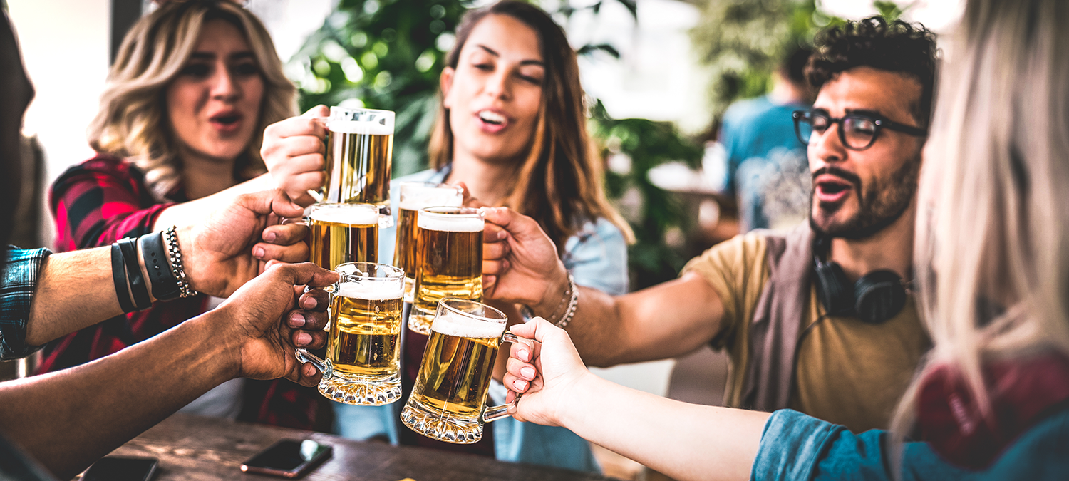 Young bar guests toasting with mugs of beer at a bar