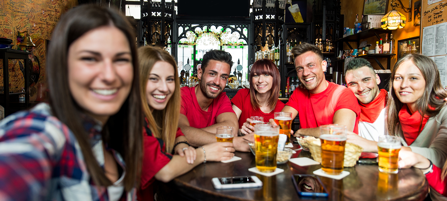Sports fans in red jerseys and shirts enjoying beers at a local sports bar