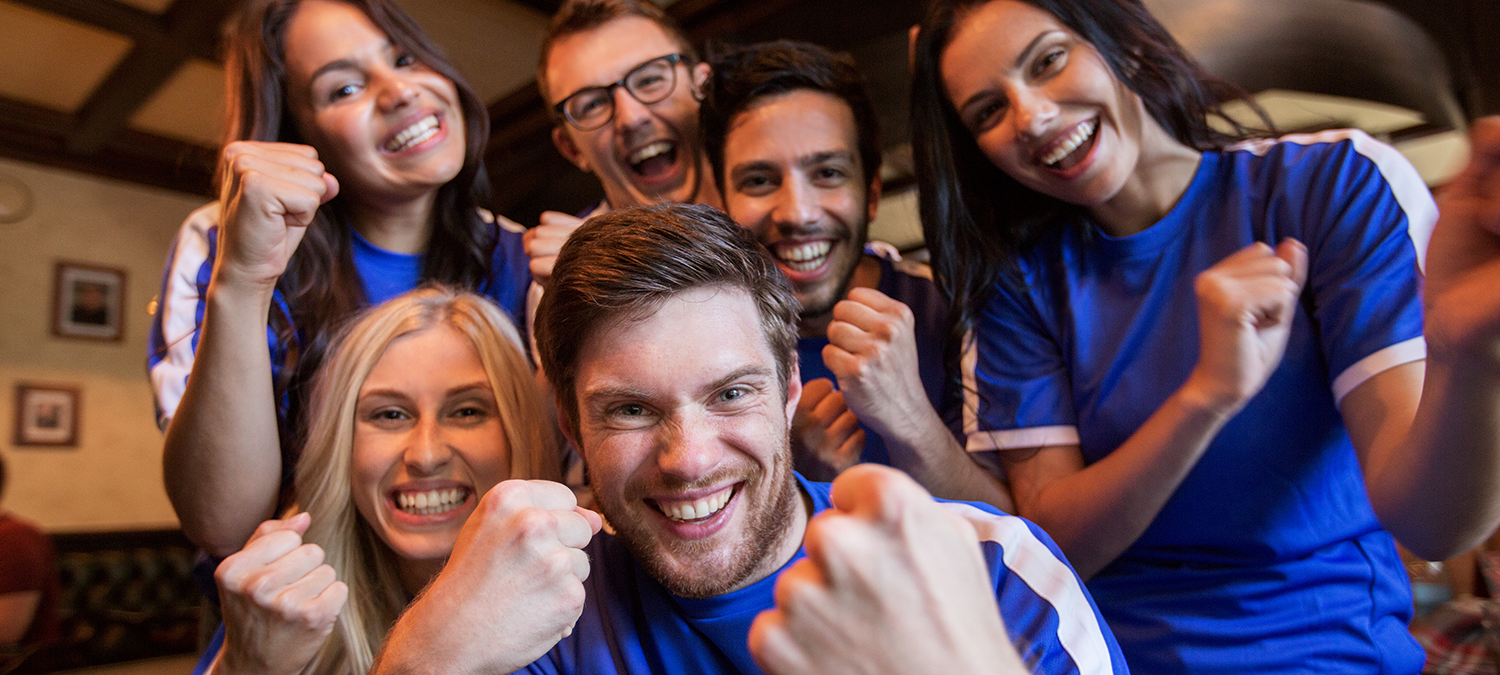 Group of sports fans in blue shirts celebrating at a local sports bar