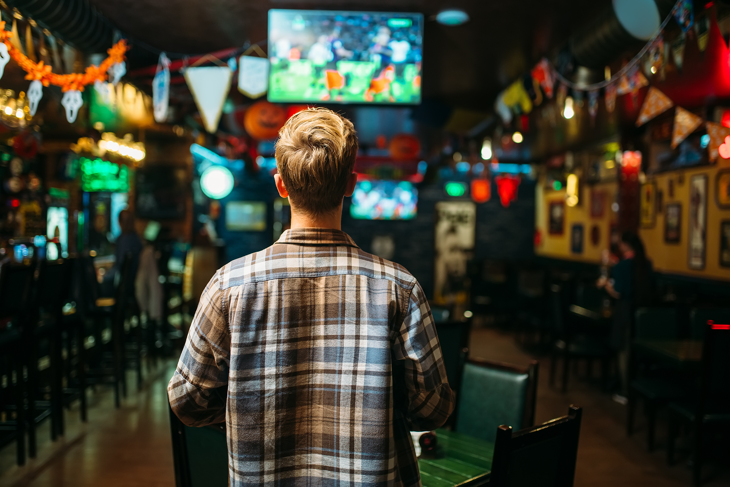 A sports fan stands in a sports bar watching a game. Several other TVs show games and matches.