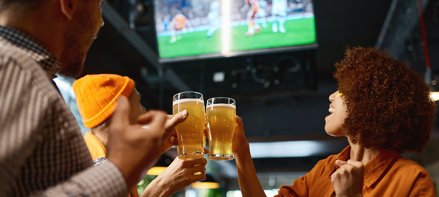 Sports fans cheering and drinking beer while watching a game on TV at a sports bar