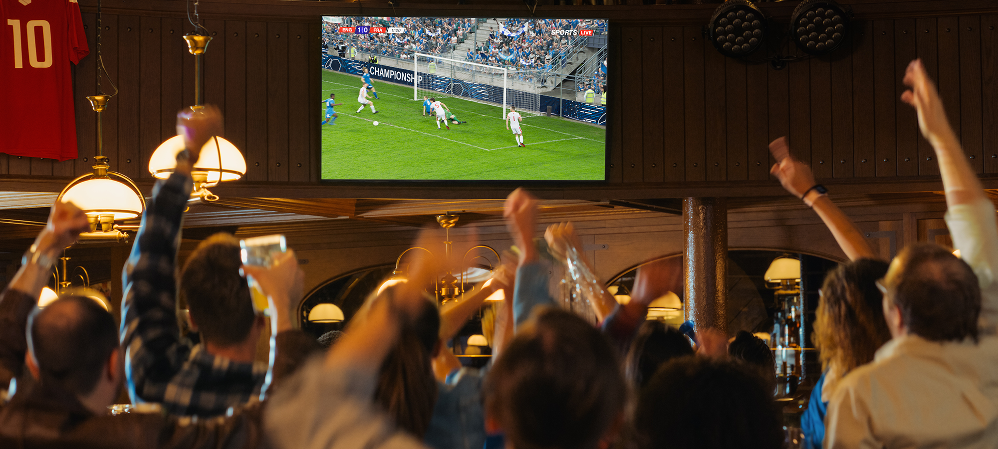 Sports fans celebrating while watching a soccer game on TV at a local sports bar.