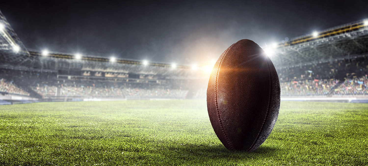 An upright football back lit by a stadium light, low angle epic show of a football arena.